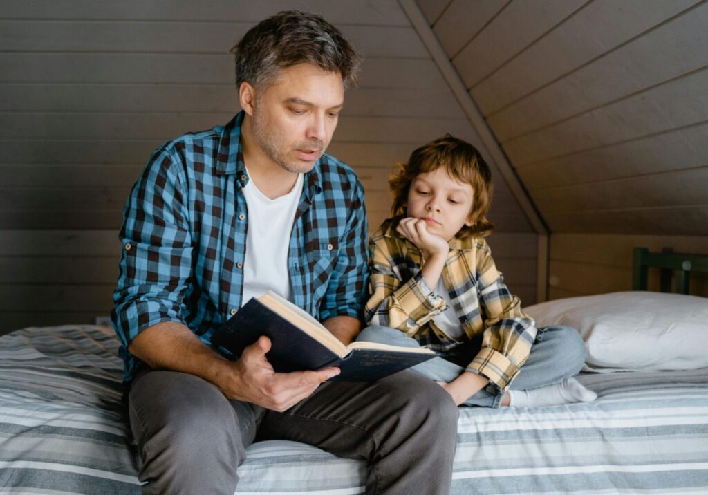 A father and son bonding while reading a book on a cozy bed.