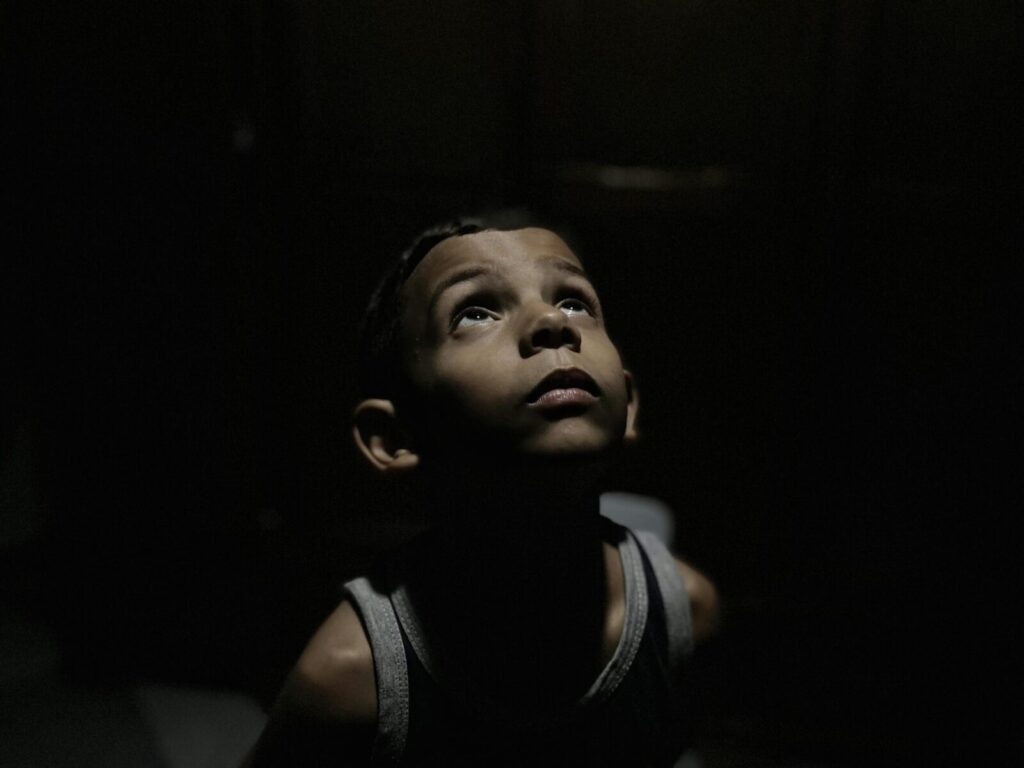 Portrait of a child looking up, seemingly contemplative, in a dimly lit environment.