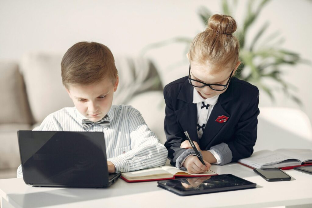 Serious business kids in formal wear taking notes in planner while working on netbook together in contemporary office behind sofa