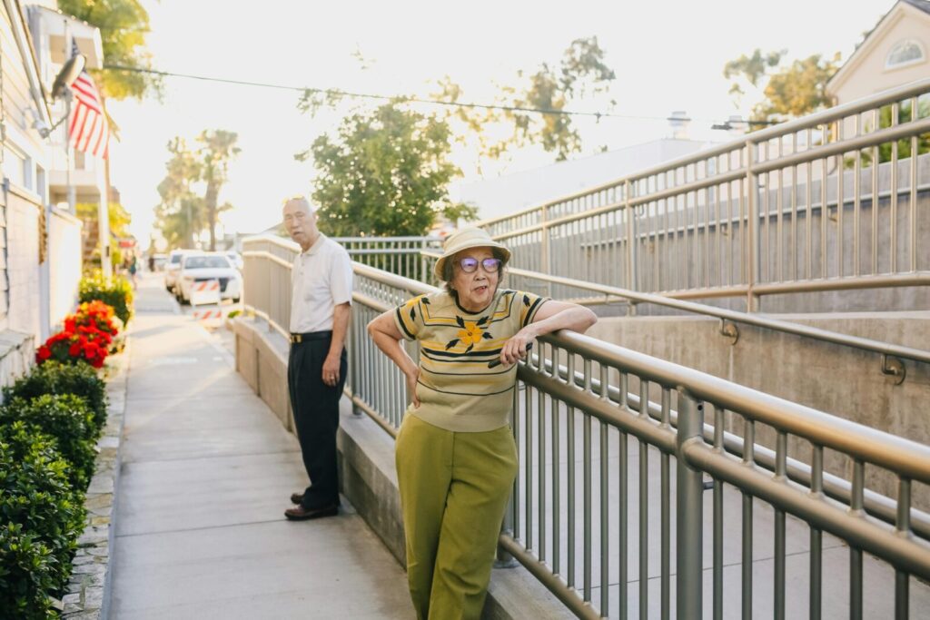 Elderly Asian couple relaxing outside near a railing during a sunny day.