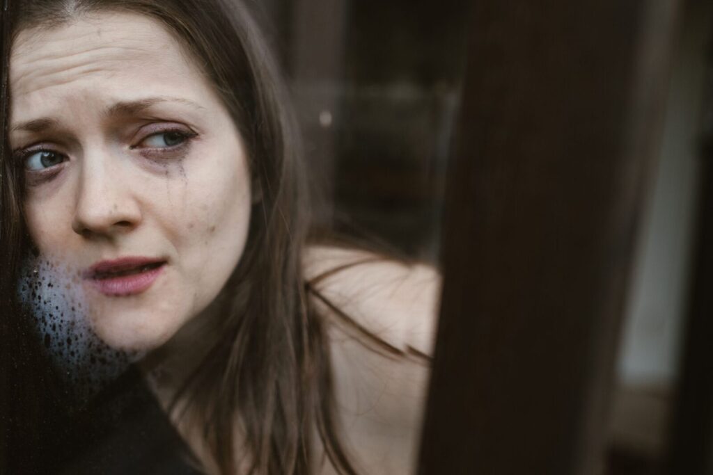 Close-up of a woman with tears gazing through a window, expressing deep emotion.
