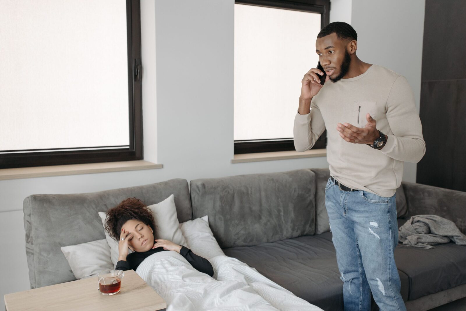 A man calls for help as a woman rests unwell on a couch at home.
