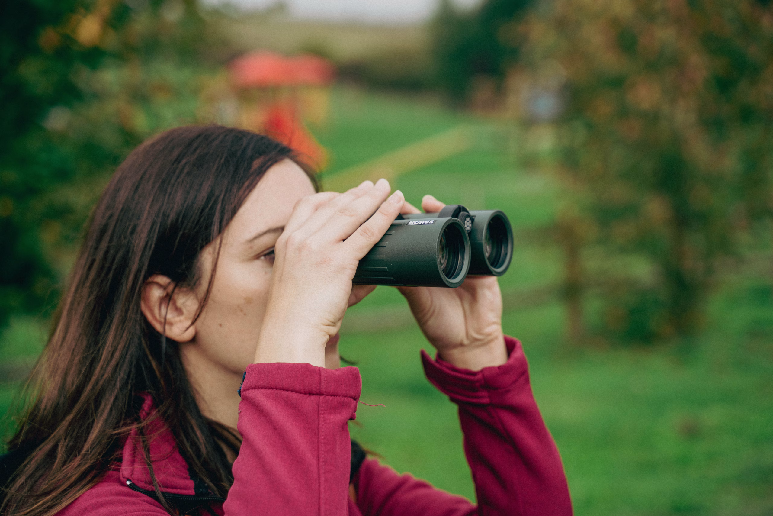 Adult woman using binoculars in a lush green setting, observing nature closely.