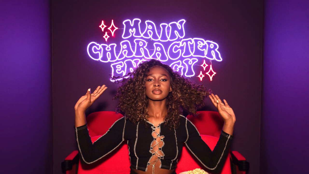 Woman with curly hair posing confidently in front of neon sign and popcorn.